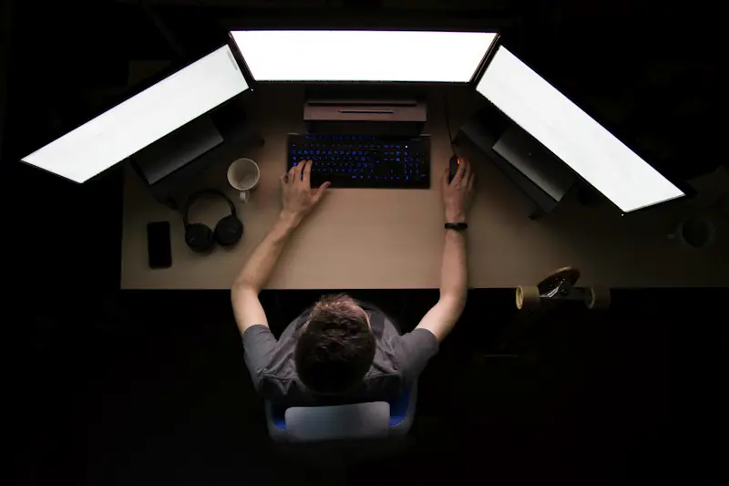 A developer at a desk between three bright screens, seen from above